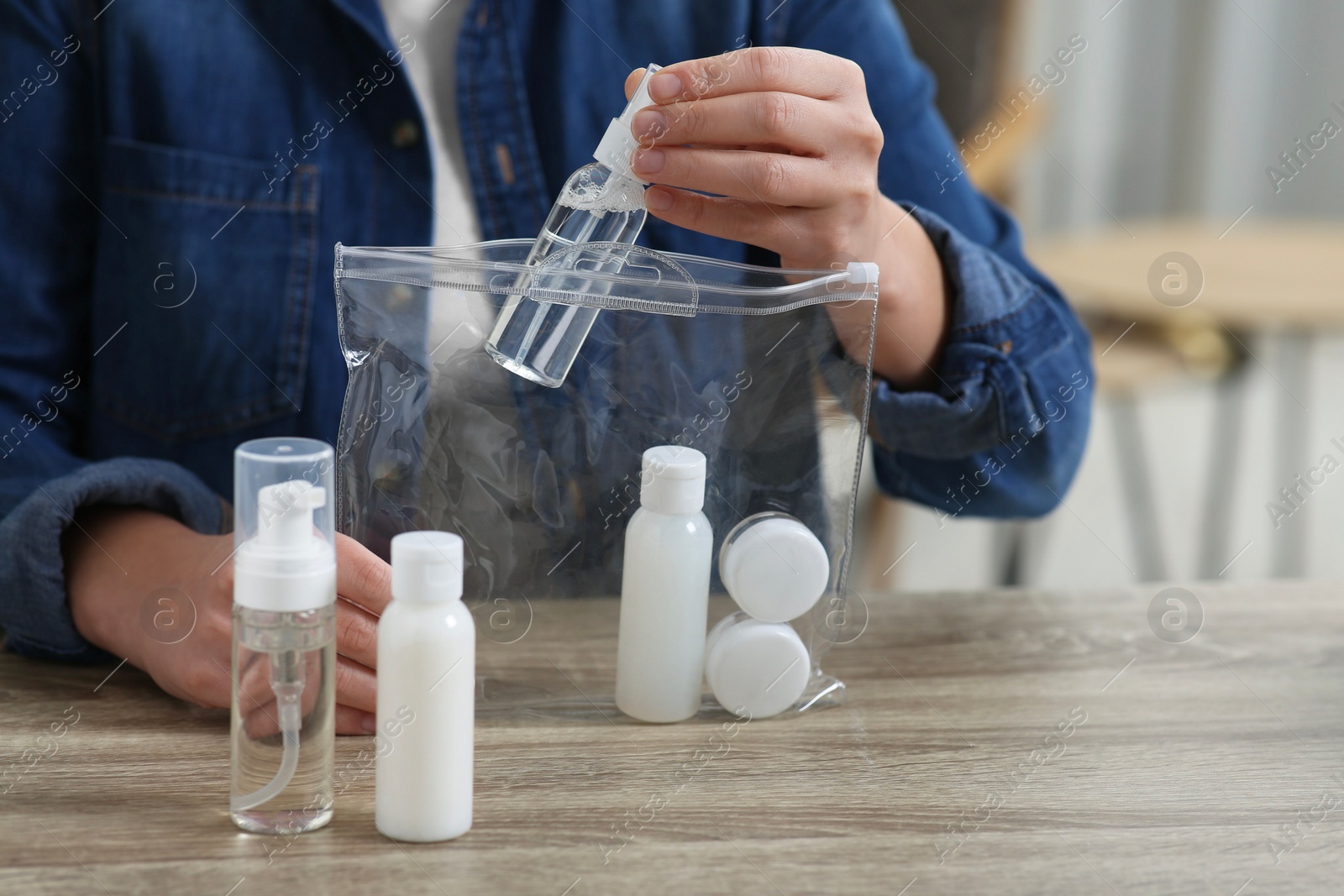 Photo of Woman packing cosmetic travel kit at wooden table indoors, closeup. Bath accessories