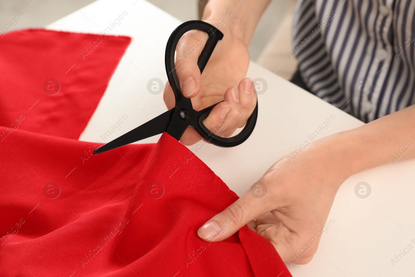 Photo of Woman cutting fabric with sharp scissors at white table, closeup