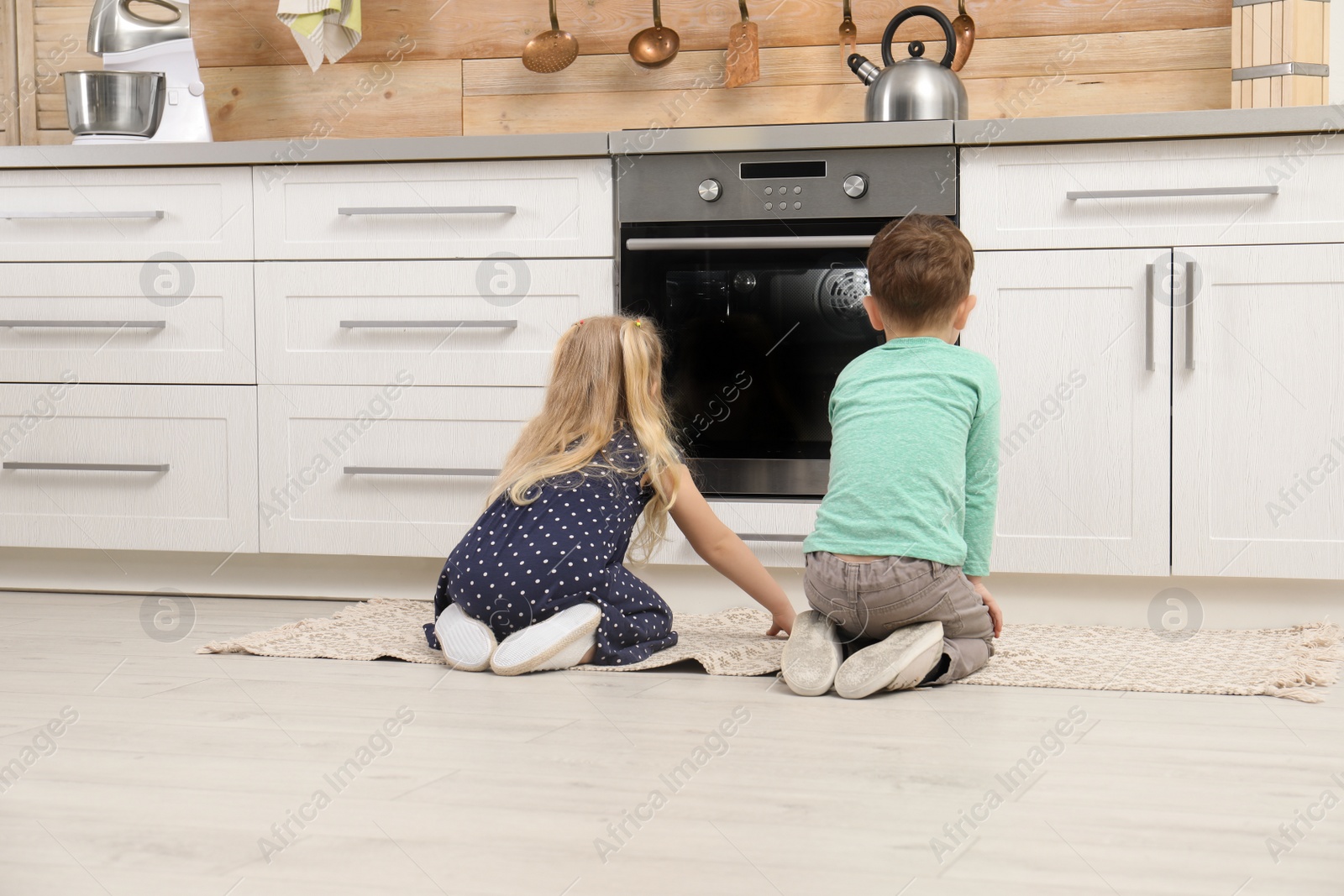 Photo of Cute children sitting near oven in kitchen