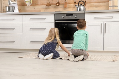 Cute children sitting near oven in kitchen