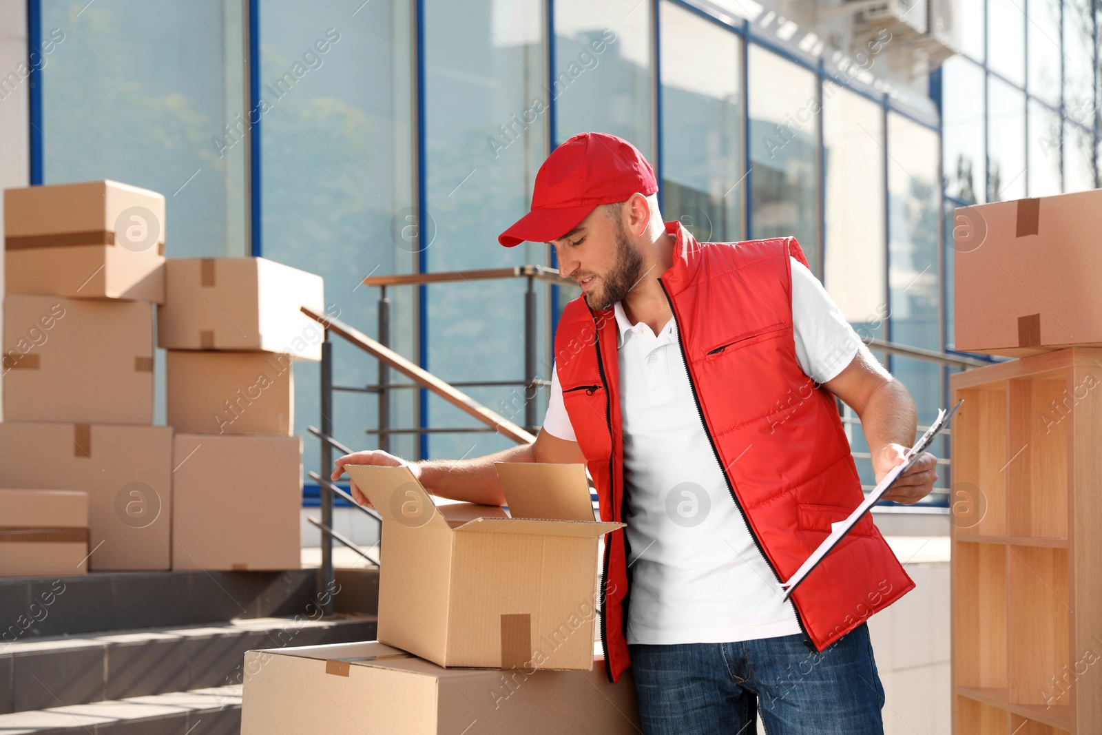 Photo of Male mover with clipboard and boxes outdoors on sunny day