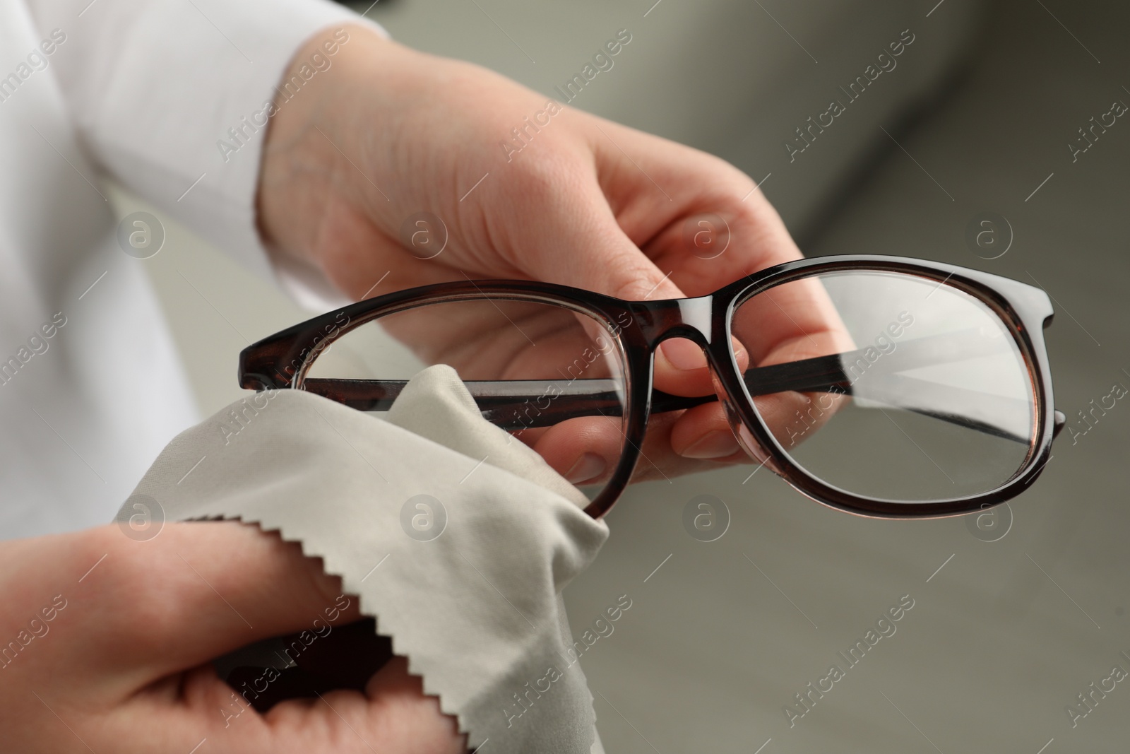 Photo of Woman cleaning glasses with microfiber cloth at home, closeup