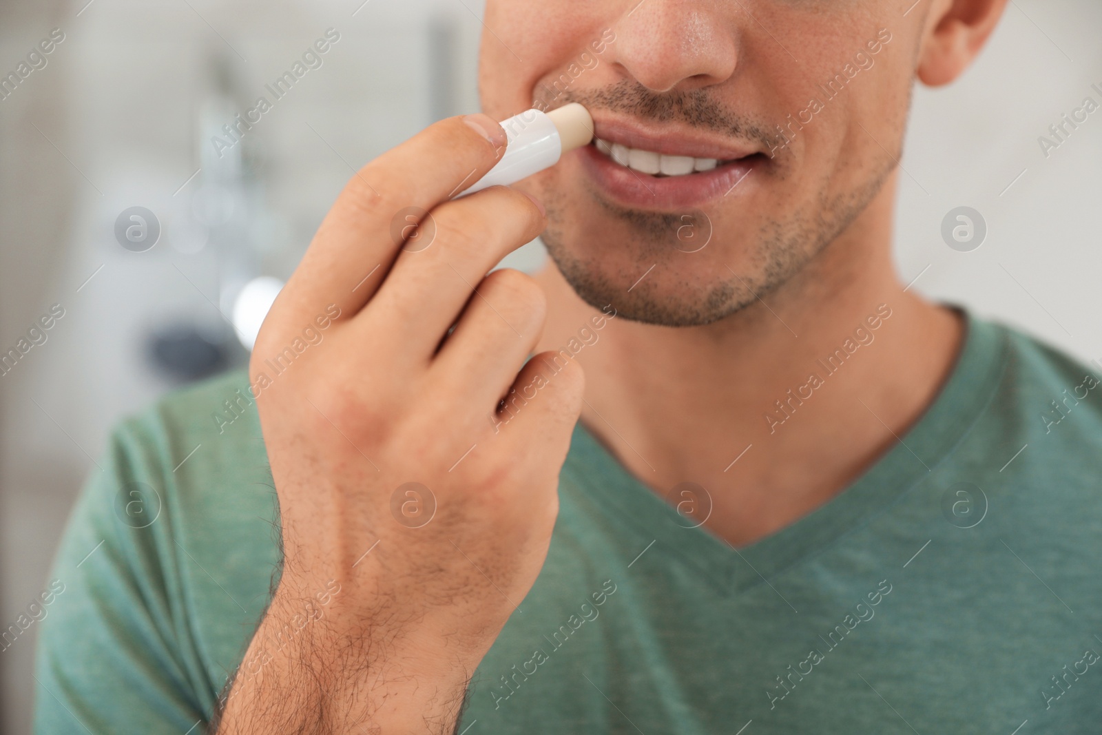 Photo of Man applying hygienic lip balm indoors, closeup