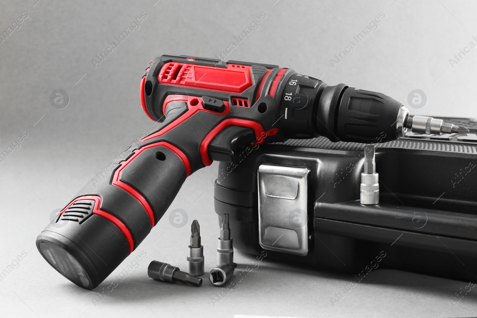 Photo of Electric screwdriver, drill bits and case on grey background, closeup