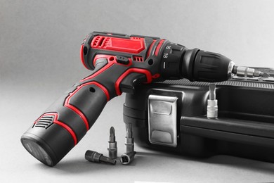 Photo of Electric screwdriver, drill bits and case on grey background, closeup