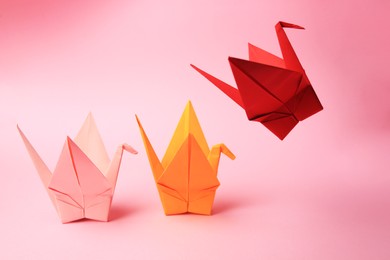 Colorful paper origami cranes on pink background