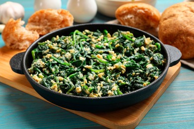 Tasty spinach dip with eggs in dish served on light blue wooden table, closeup