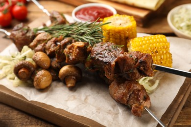 Metal skewers with delicious meat and vegetables served on wooden table, closeup