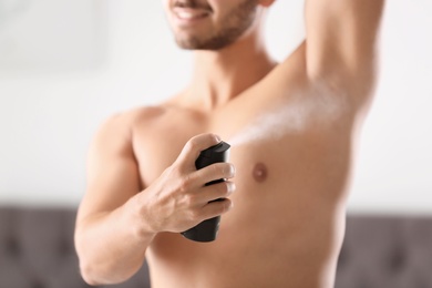 Photo of Handsome young man applying deodorant in room