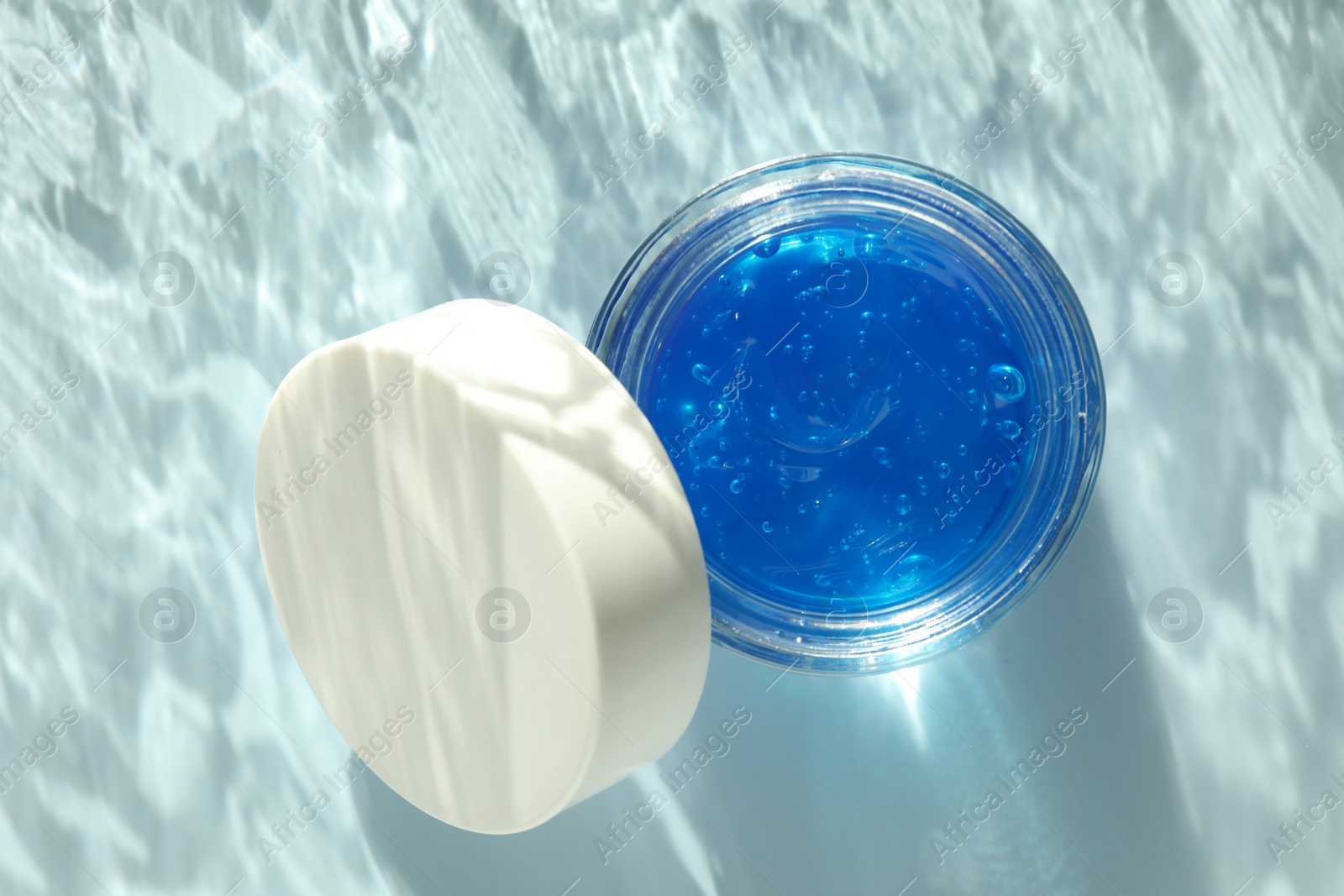 Photo of Open jar of cosmetic product on light blue background, top view