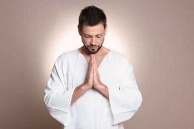 Photo of Religious man with clasped hands praying against grey background