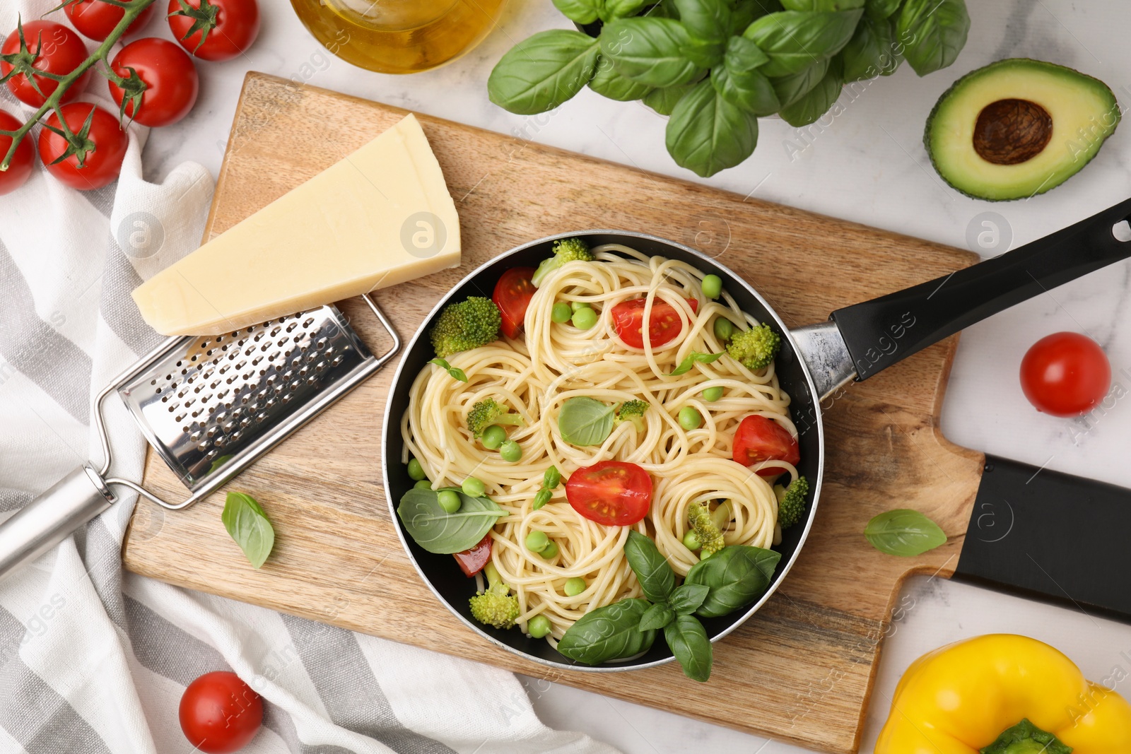 Photo of Delicious pasta primavera in frying pan and ingredients on white table, flat lay