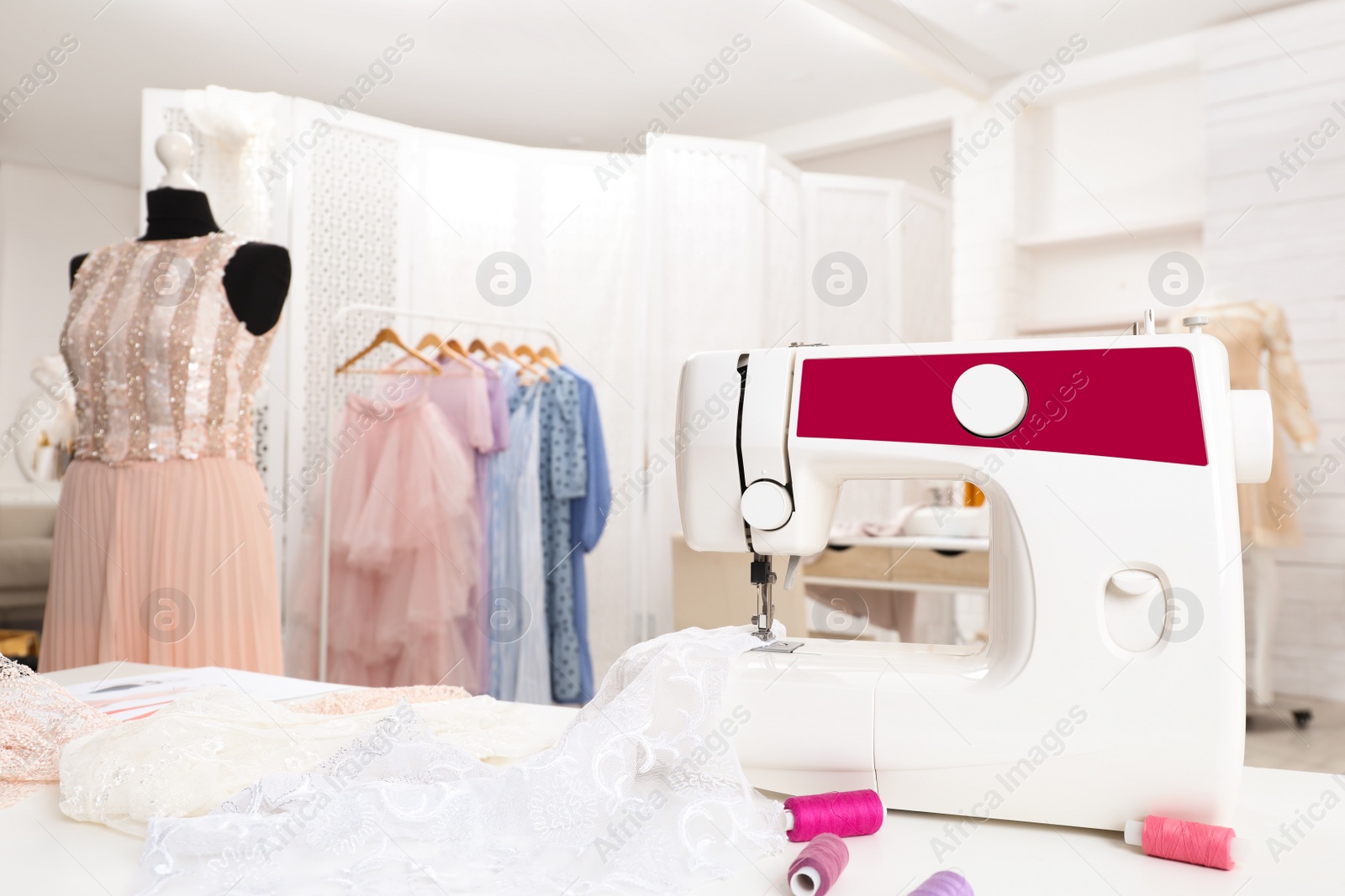 Photo of Modern sewing machine with fabric and bright threads on table in dressmaking workshop