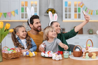 Family making selfie while painting Easter eggs at table in kitchen