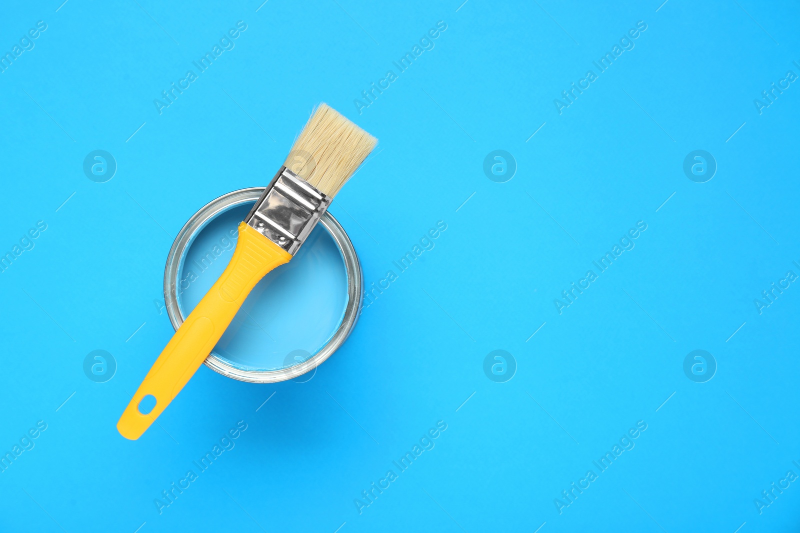Photo of Can of paint with brush on light blue background, top view. Space for text