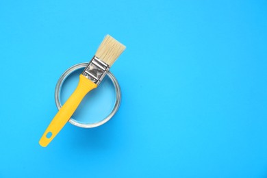 Photo of Can of paint with brush on light blue background, top view. Space for text