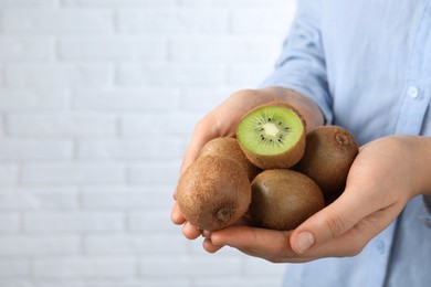 Woman holding pile of fresh ripe kiwis against white brick wall, closeup. Space for text