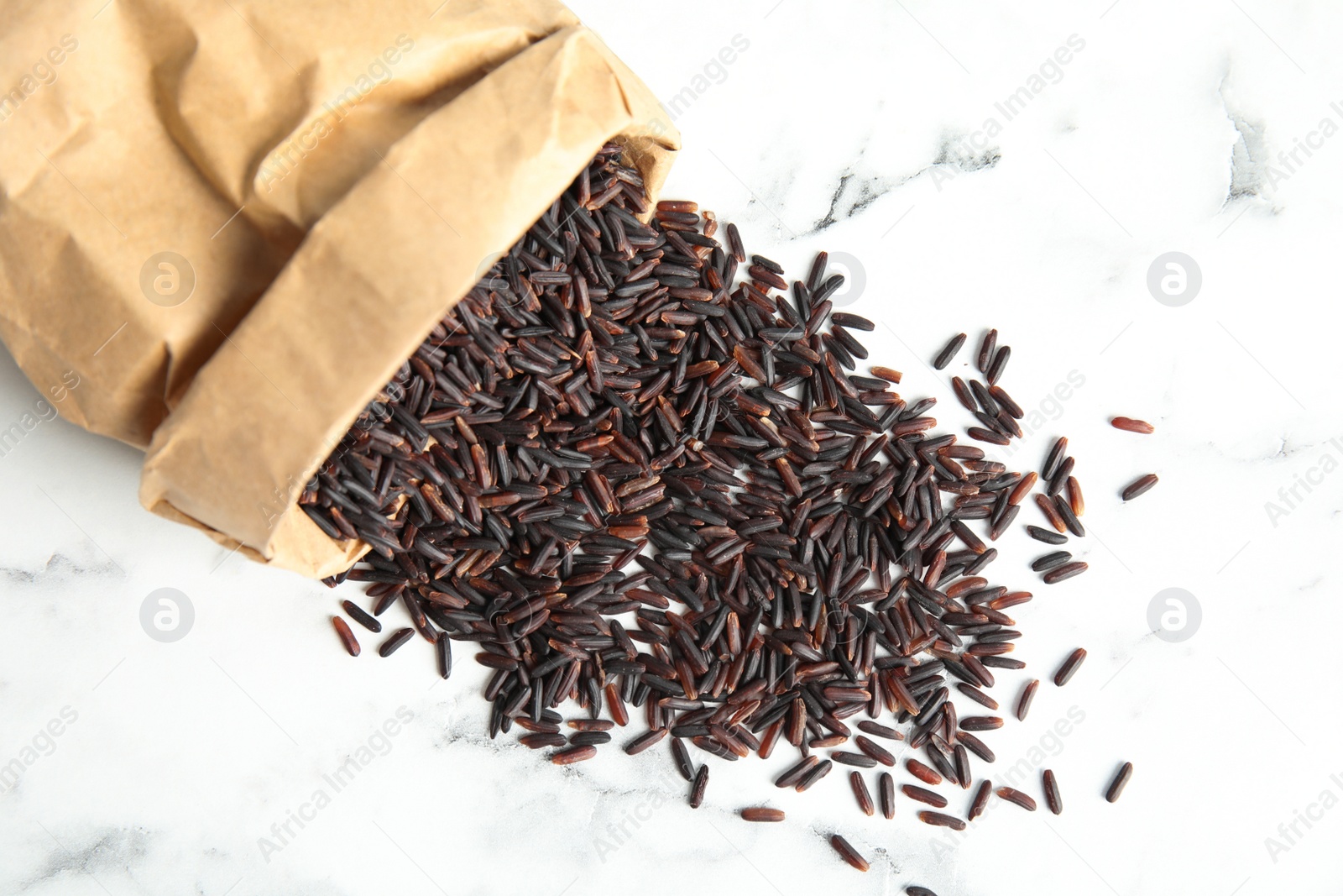 Photo of Paper bag with uncooked black rice on marble background, top view