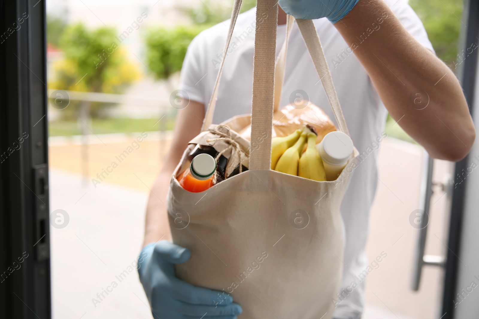 Photo of Male volunteer giving bag with products through doorway, closeup. Aid during coronavirus quarantine