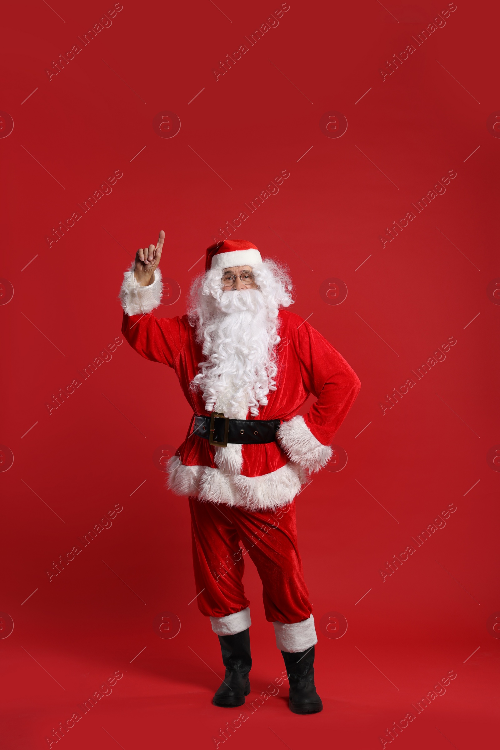 Photo of Merry Christmas. Santa Claus pointing at something on red background