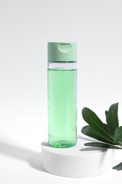 Photo of Bottle with cosmetic product and green leaves on white background