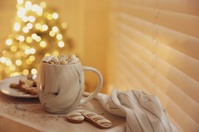 Photo of Tasty hot drink with marshmallows against Christmas lights. Space for text