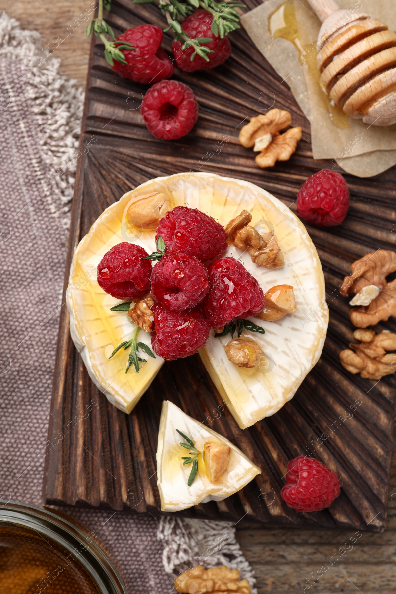 Photo of Brie cheese served with raspberries, walnuts and honey on wooden table, flat lay