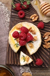 Photo of Brie cheese served with raspberries, walnuts and honey on wooden table, flat lay