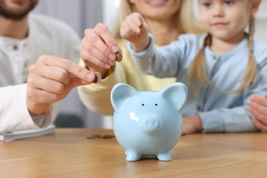 Photo of Planning budget together. Little girl with her family putting coins into piggybank at table, closeup