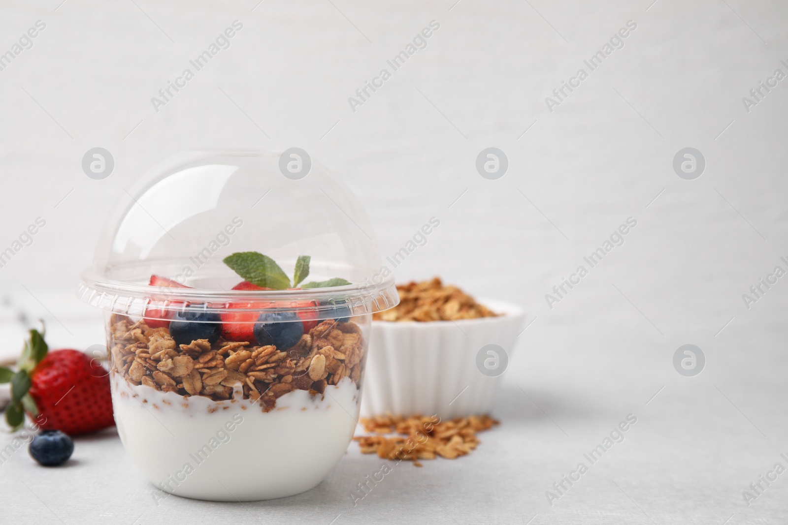 Photo of Tasty granola with berries and yogurt in plastic cup on light table, space for text