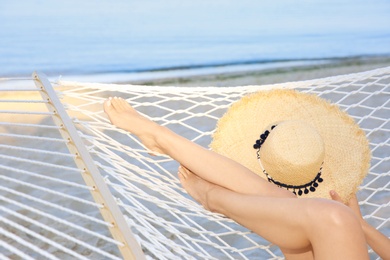 Photo of Young woman with straw hat resting in hammock at seaside. Summer vacation