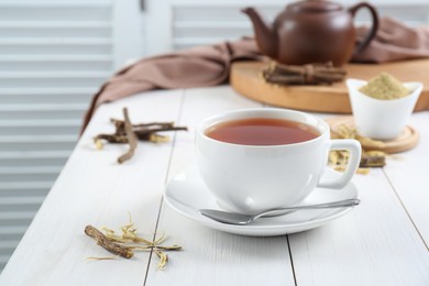 Aromatic licorice tea in cup and dried sticks of licorice root on white wooden table. Space for text