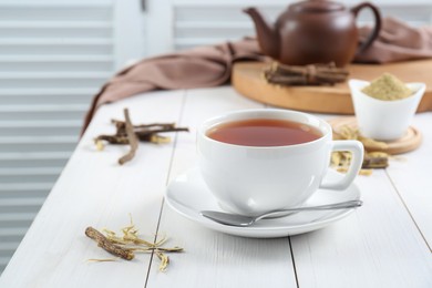 Photo of Aromatic licorice tea in cup and dried sticks of licorice root on white wooden table. Space for text