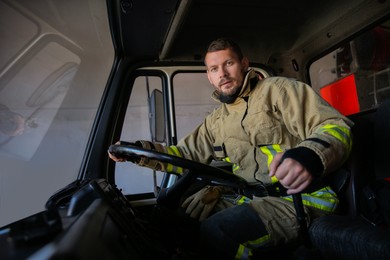 Photo of Firefighter in uniform driving modern fire truck