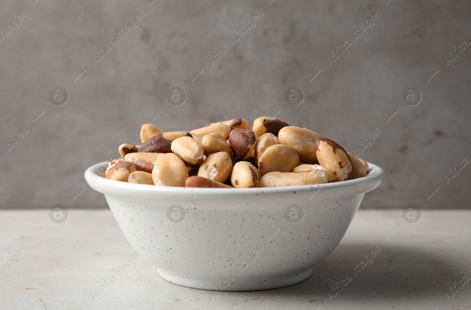 Photo of Bowl with tasty Brazil nuts on grey table