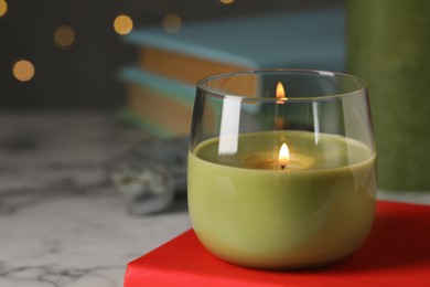 Photo of Burning candle and book on white marble table, space for text