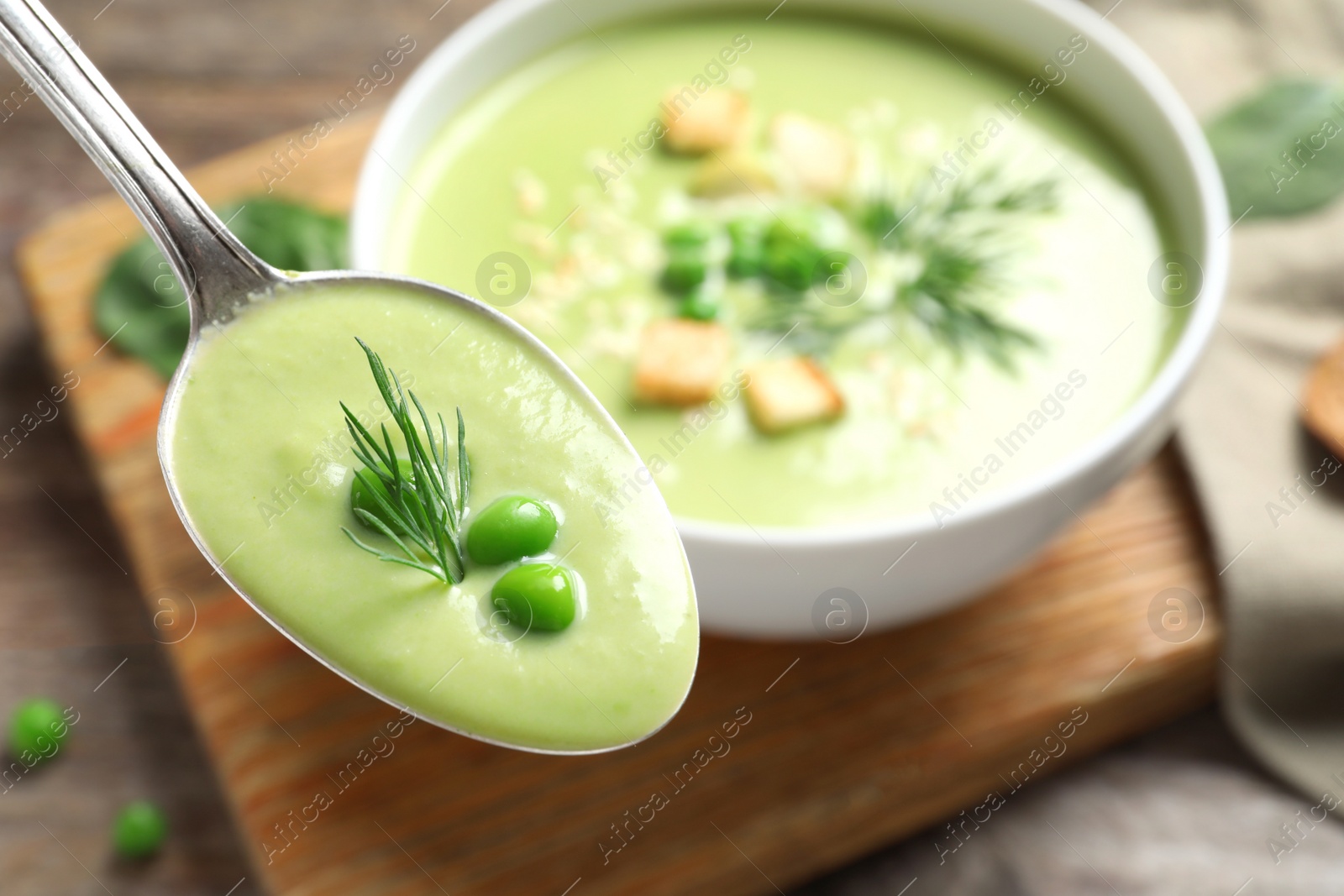 Photo of Spoon with fresh vegetable detox soup made of green peas on blurred background, closeup