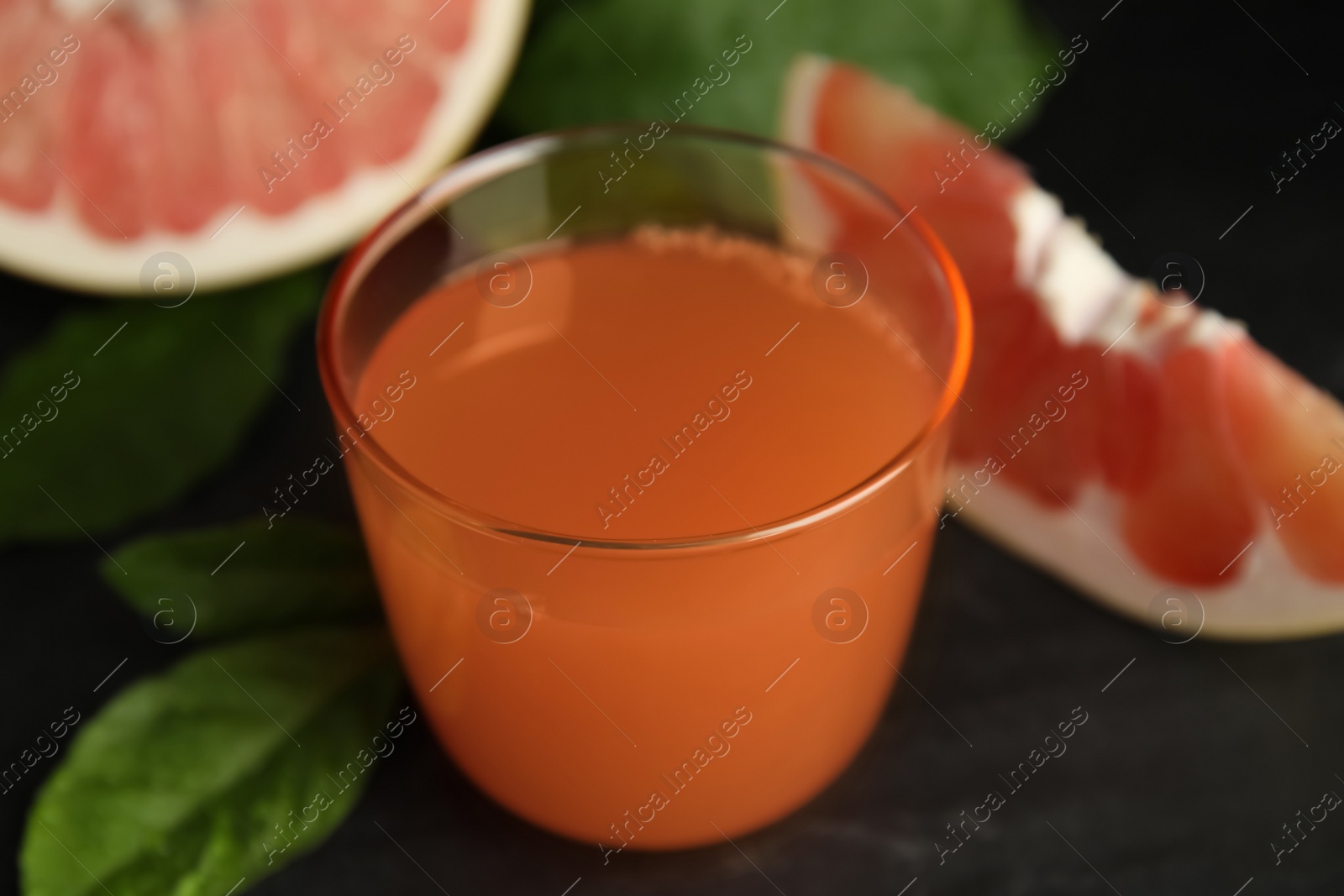 Photo of Glass of pink pomelo juice and green leaves on black table, closeup