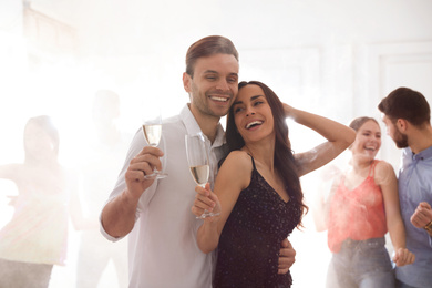 Lovely young couple with glasses of champagne at dancing party
