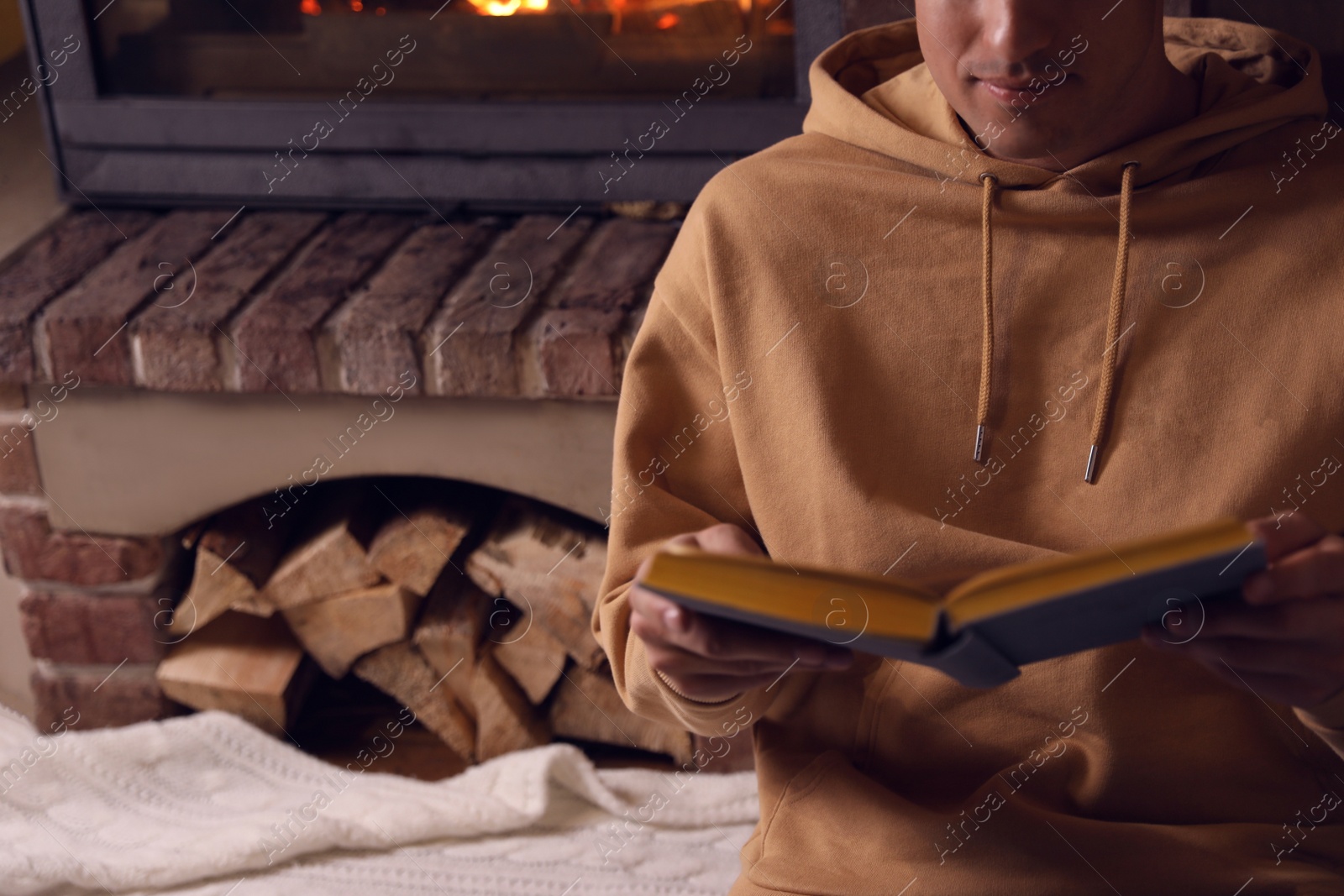 Photo of Man reading book near fireplace at home, closeup