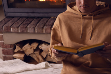 Man reading book near fireplace at home, closeup