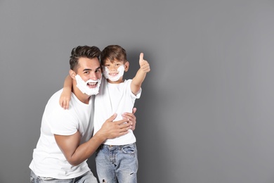 Photo of Father and son with shaving foam on faces against color background. Space for text