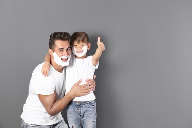 Father and son with shaving foam on faces against color background. Space for text