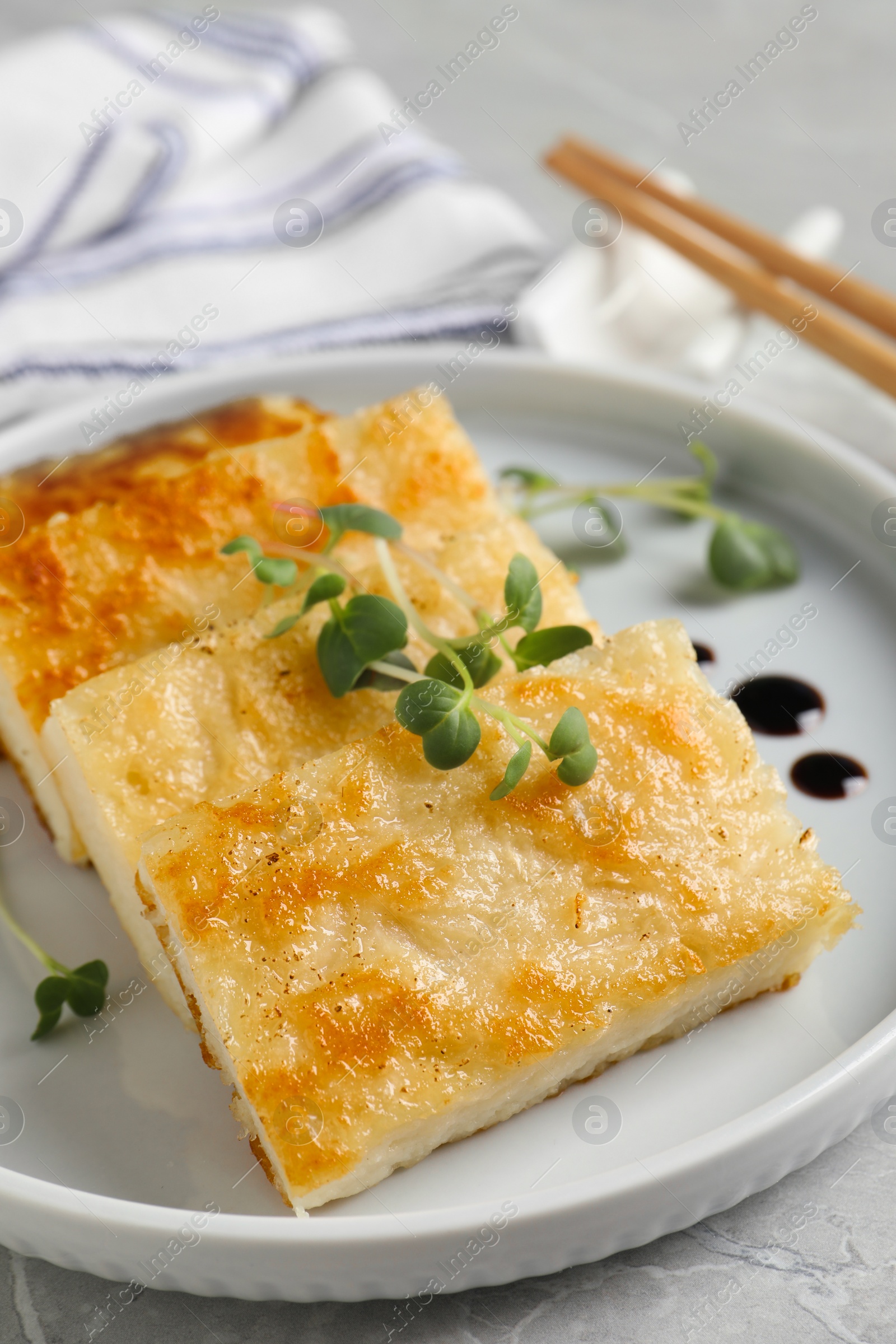 Photo of Delicious turnip cake with microgreens served on grey table, closeup