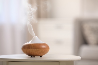 Photo of Modern essential oil diffuser on table indoors. Space for text