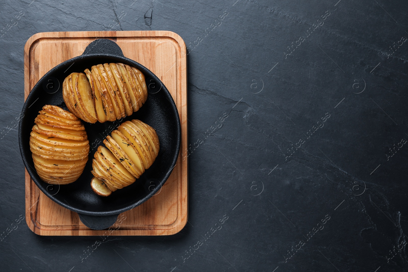 Photo of Delicious homemade Hasselback potatoes on black table, top view. Space for text
