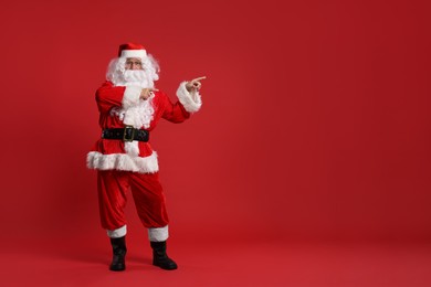 Merry Christmas. Santa Claus pointing at something on red background, space for text