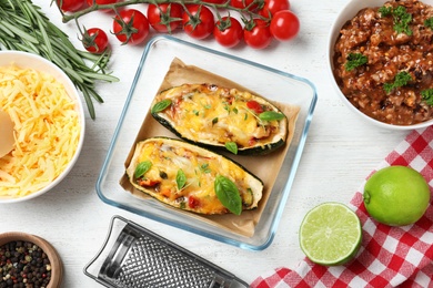 Photo of Baked stuffed zucchini with ingredients on white wooden background, flat lay