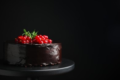 Tasty homemade chocolate cake with berries and rosemary on dessert stand against black background. Space for text