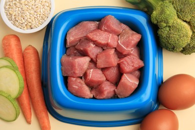 Photo of Raw meat in bowl and healthy products for pet on beige background, flat lay
